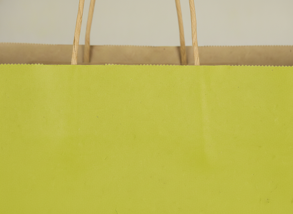 Macro detail of the twisted handle and folded edge of an avocado green kraft bag