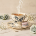 Blue rose garden teacup filled with steaming tea beside macarons and roses on a styled marble table