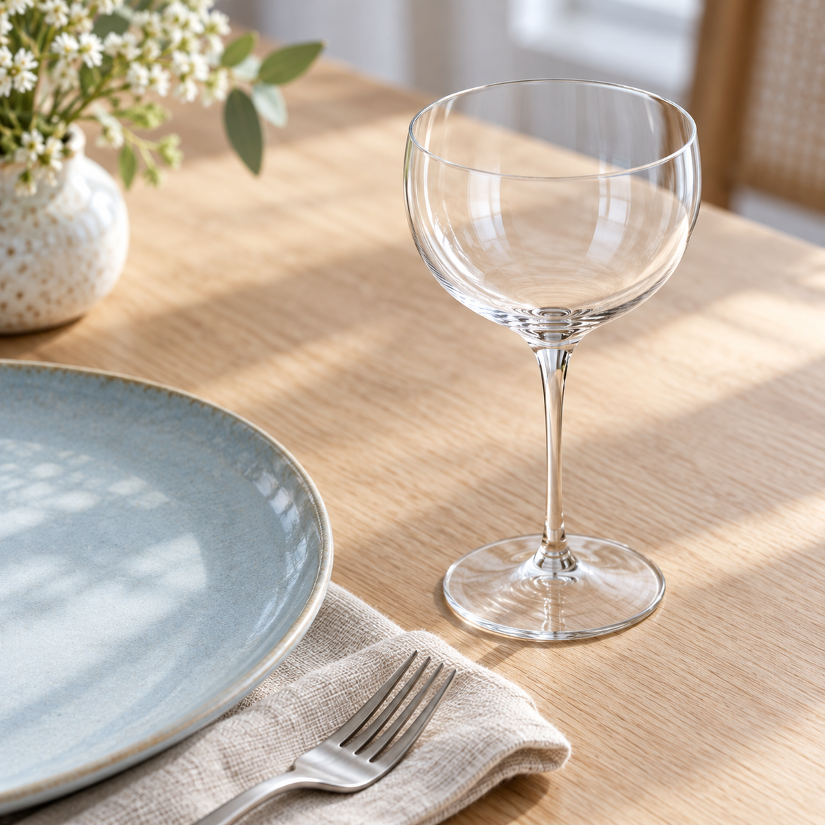 Clear rounded cocktail glass at a daylight lunch setting with a blue ceramic plate