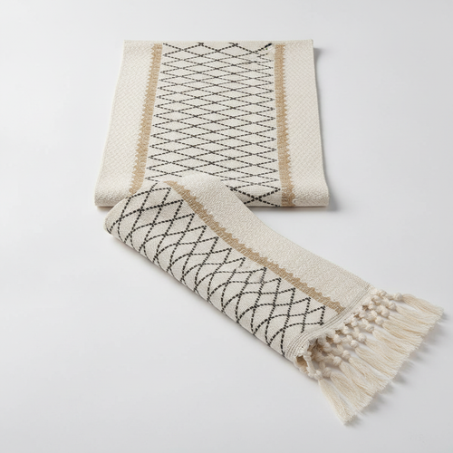 Woven boho cotton table runner in black and beige with diamond lattice pattern and cream tassels, studio packshot