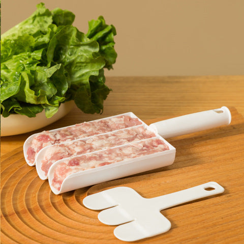 White three-channel meatball scoop filled with minced meat beside its three-prong paddle on a wooden board