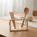 Glass and wood utensil holder holding chopsticks and a wooden spoon on a dining table