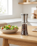Pepper grinder on a kitchen table beside a salad bowl