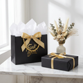 Black gift bag with gold bow styled on a marble table with gift and florals