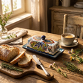 Artisan floral ceramic butter dish on a breakfast table with bread, butter knife, herbs and coffee