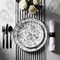 Dramatic black and white dinner table setting with monochrome disposable plates, matte black cutlery, white roses, and crystal glassware