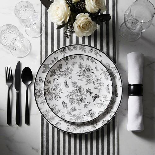 Dramatic black and white dinner table setting with monochrome disposable plates, matte black cutlery, white roses, and crystal glassware