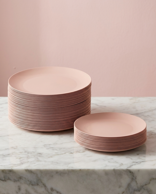 Full set of blush disposable dinnerware plates stacked on marble with soft pink backdrop