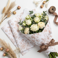 Floral Essence coffee vintage floral wrapping paper sheets fanned open with a wrapped flower bouquet, ribbon and dried botanicals on white surface