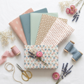 Boho Chic pink and blue patterned tissue paper sheets fanned with a wrapped gift box topped with tissue blooms and dried flowers on linen