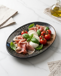 Oval reactive speckled charcoal-amber glaze porcelain serving platter with antipasto on white marble