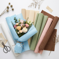 Artisan wrinkled flower wrapping paper rolls and sheets in multiple colors fanned with a bouquet wrapped in one color, scissors and dried botanicals on white surface