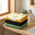 Yellow, black and green cotton face towels folded on wood shelf with succulent and soap pump