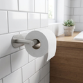Brushed stainless steel self-adhesive toilet paper holder mounted on white bathroom tile wall with small plant
