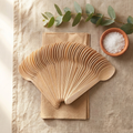 150-pack EcoSpoon natural birch wooden disposable spoons fanned out on rustic linen placemat with eucalyptus accents
