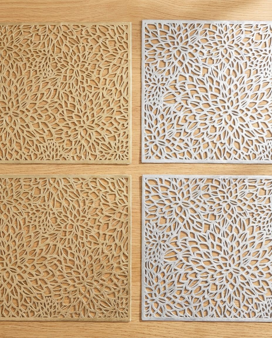 Overhead flat-lay of all 4 laser-cut nature placemats showing 2 gold and 2 silver metallic botanical designs side by side on wood table