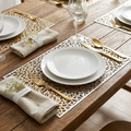 Laser-cut gold botanical placemats styled in an elegant place setting with white plates, gold cutlery, wine glass, and baby's breath florals