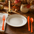 Autumn place setting with a white plate and orange plastic cutlery on a warm oak table