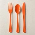 Orange plastic fork, spoon and knife laid side by side on a warm off-white speckled surface