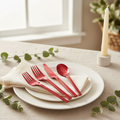 Red disposable plastic cutlery set on a cream napkin and white plate at an elegant candlelit place setting