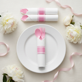 Pre-rolled pink plastic cutlery in a white napkin with a pink band on a white plate at a baby shower setting