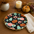 Halloween place setting on a warm oak table with the scalloped black pumpkin plate and a folded cream linen napkin