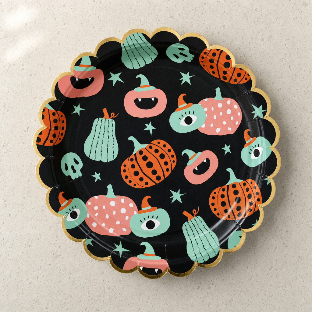 A single round scalloped Halloween paper plate face-up, matte black with coral, mint and orange pumpkins and a gold foil scalloped rim