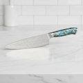 Damascus-pattern chef knife with iridescent abalone-resin handle on a marble counter