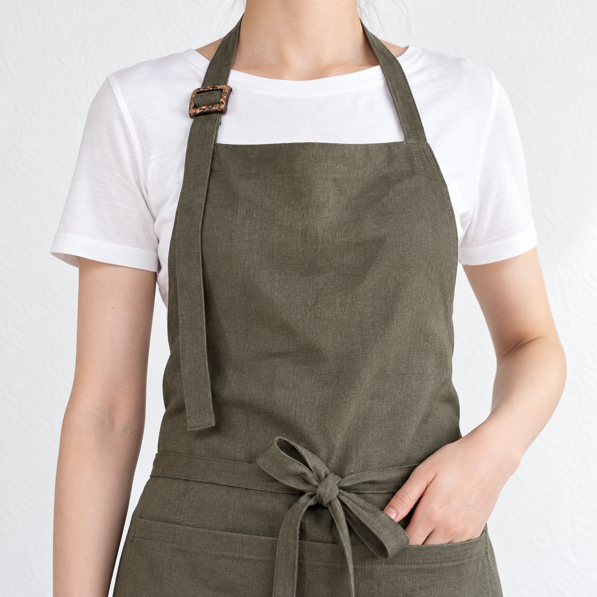 AI-derived close view of the olive green apron's front neck strap and square buckle. Clothing and styling props are not included.