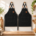 Two matching black three-pocket aprons displayed front-facing together. Kitchen decor is styling only.