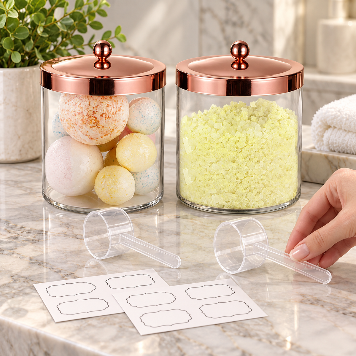 Two closed rose-gold-lid jars with clear scoops and sample blank labels being arranged; hand, bath contents and bathroom decor are styling props, not included.