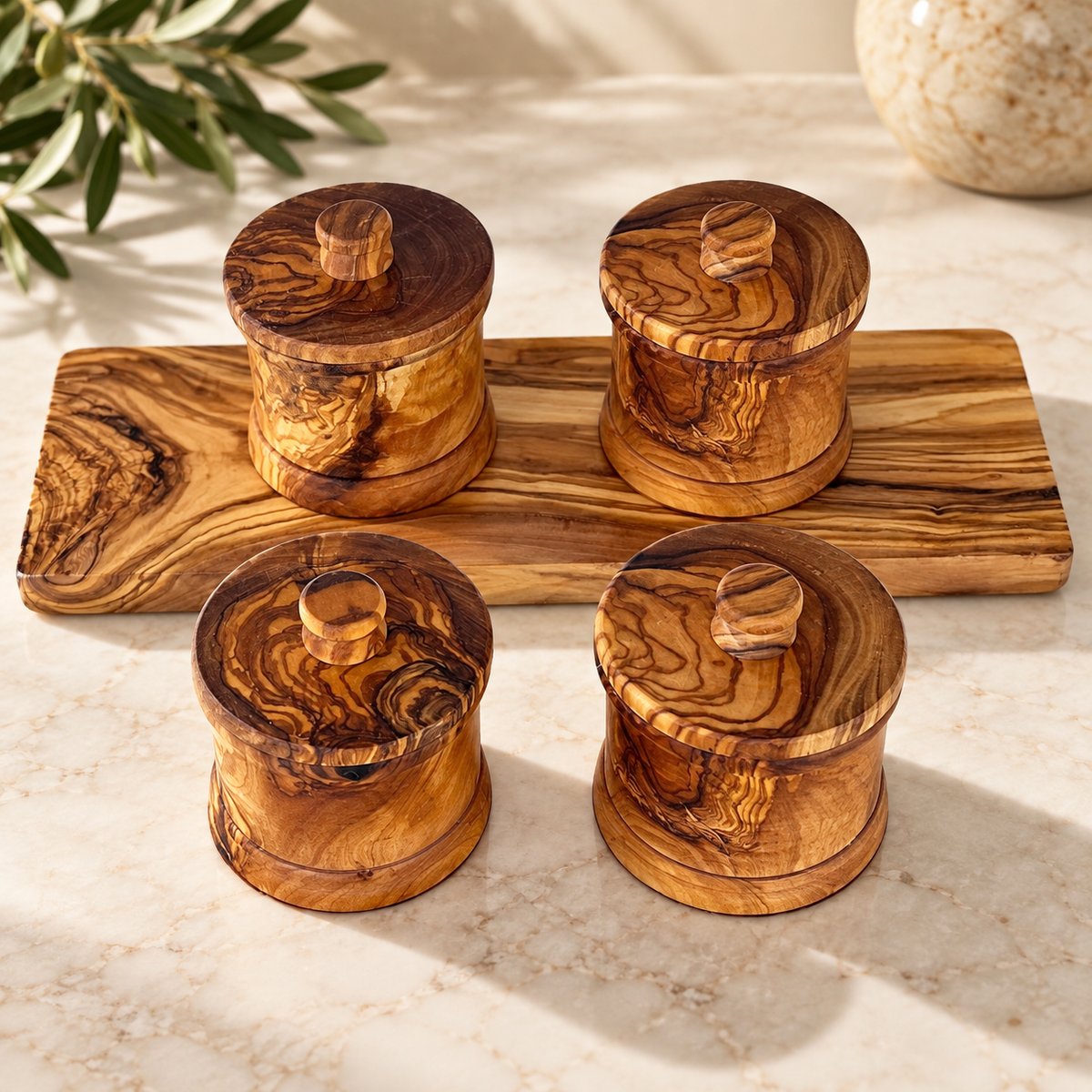New close view of four closed canisters and matching tray, showing knobs and exterior rings; leaves and tabletop are styling props, not included.