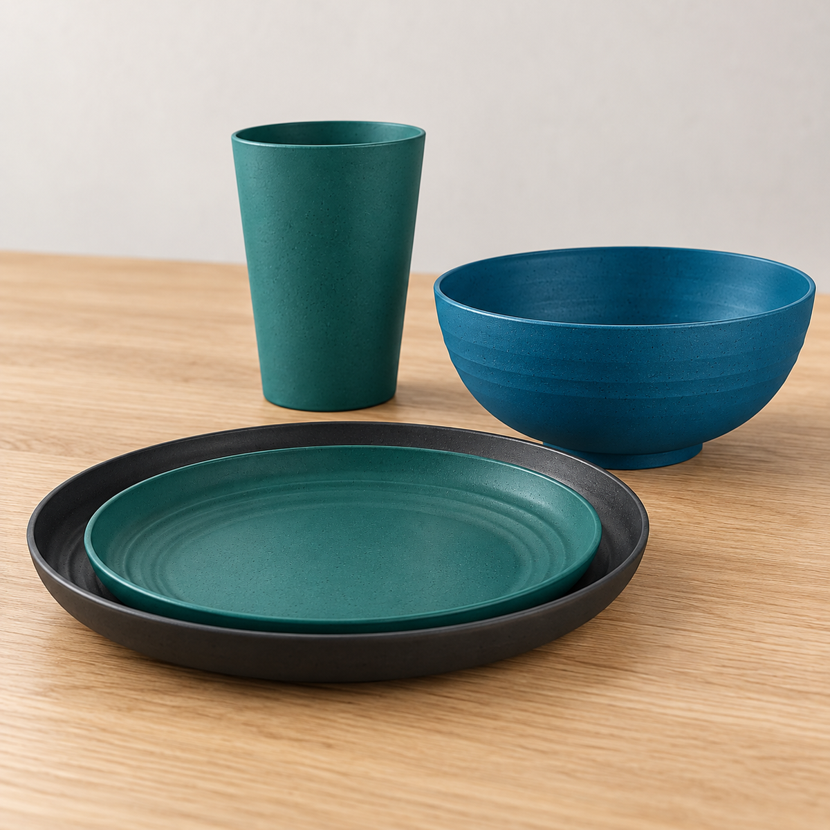 Low oblique detail of charcoal and teal plate rims with a petrol-blue footed bowl and teal tumbler. Empty sample arrangement.