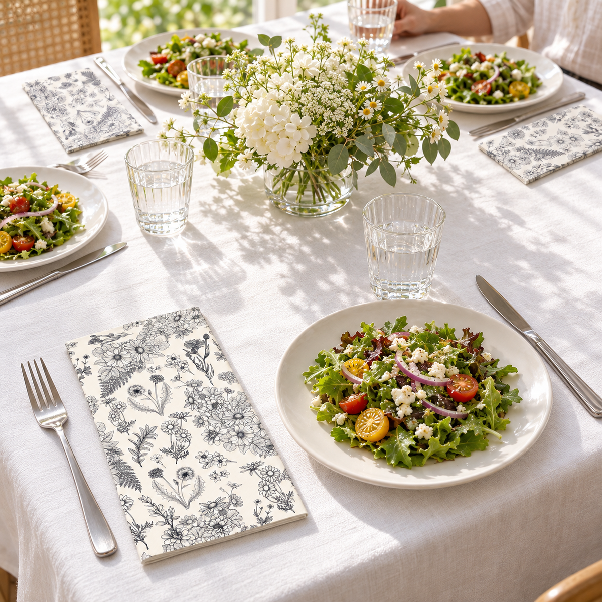 Black and white botanical paper guest napkins in a four-guest dining table. Other tableware, food and decor are styling props, not included.