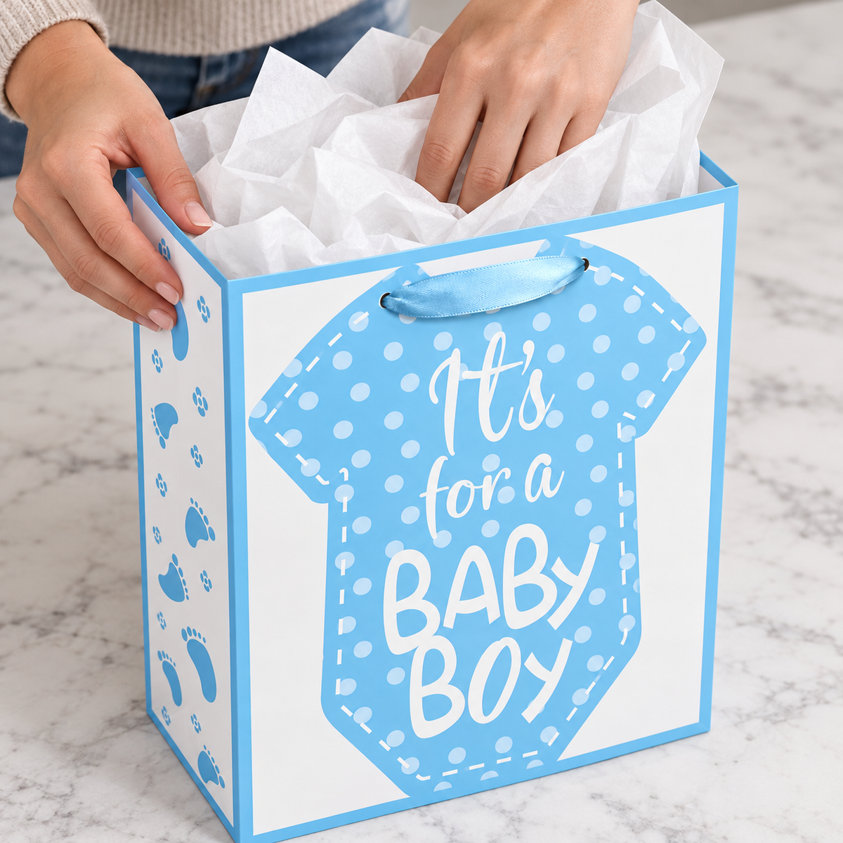 Blue Baby Boy Gift Bag with Card with tissue being placed into the opening from a high angle
