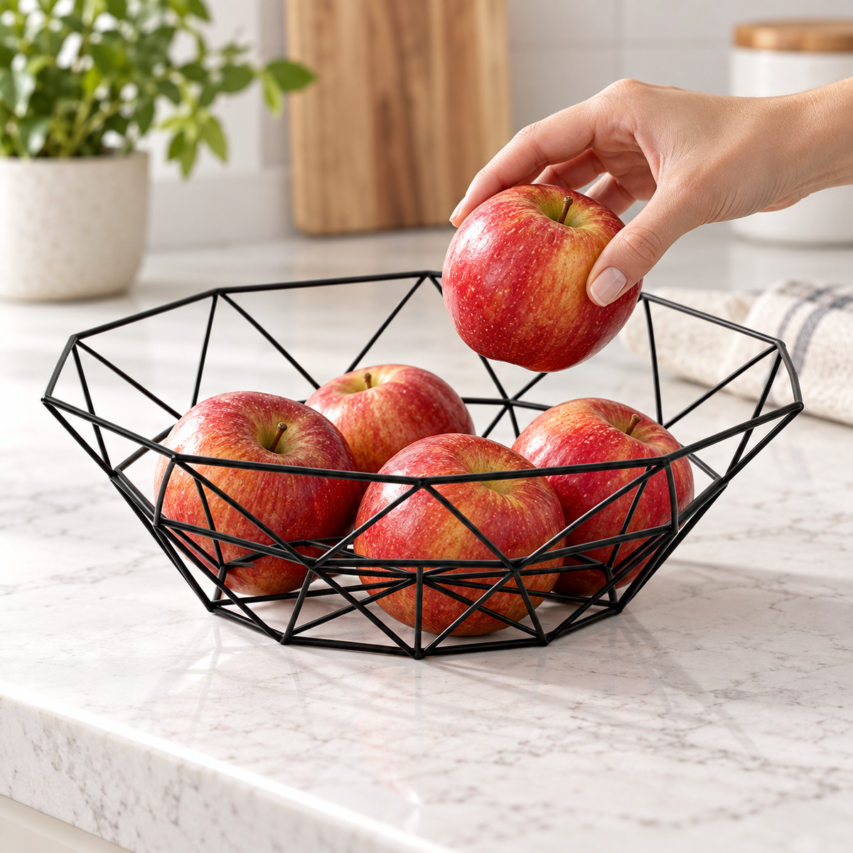 Hand lifting apple from black geometric wire basket; fruit not included