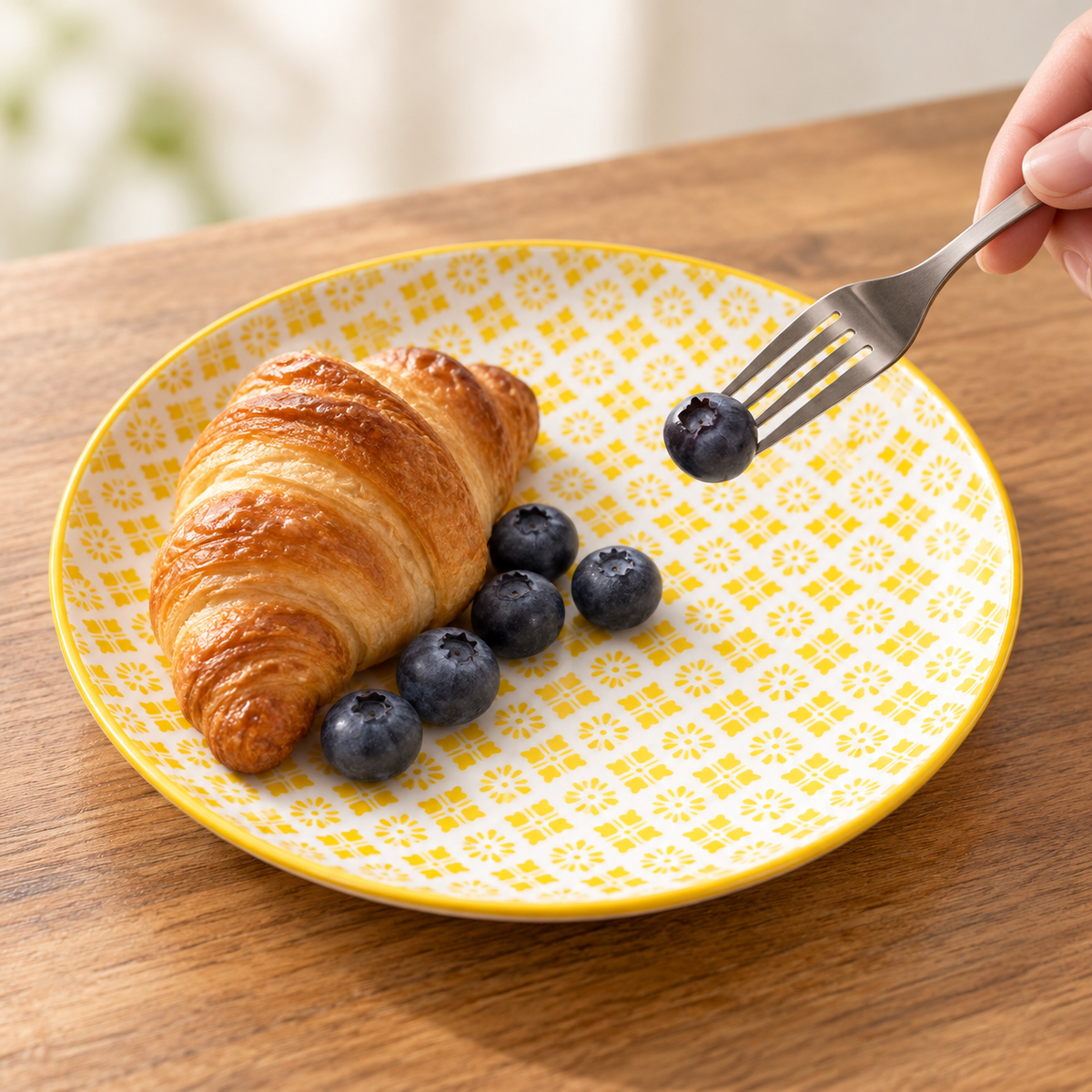 The yellow patterned ceramic plate used for breakfast with a croissant and blueberries. Food and fork are styling props, not included.