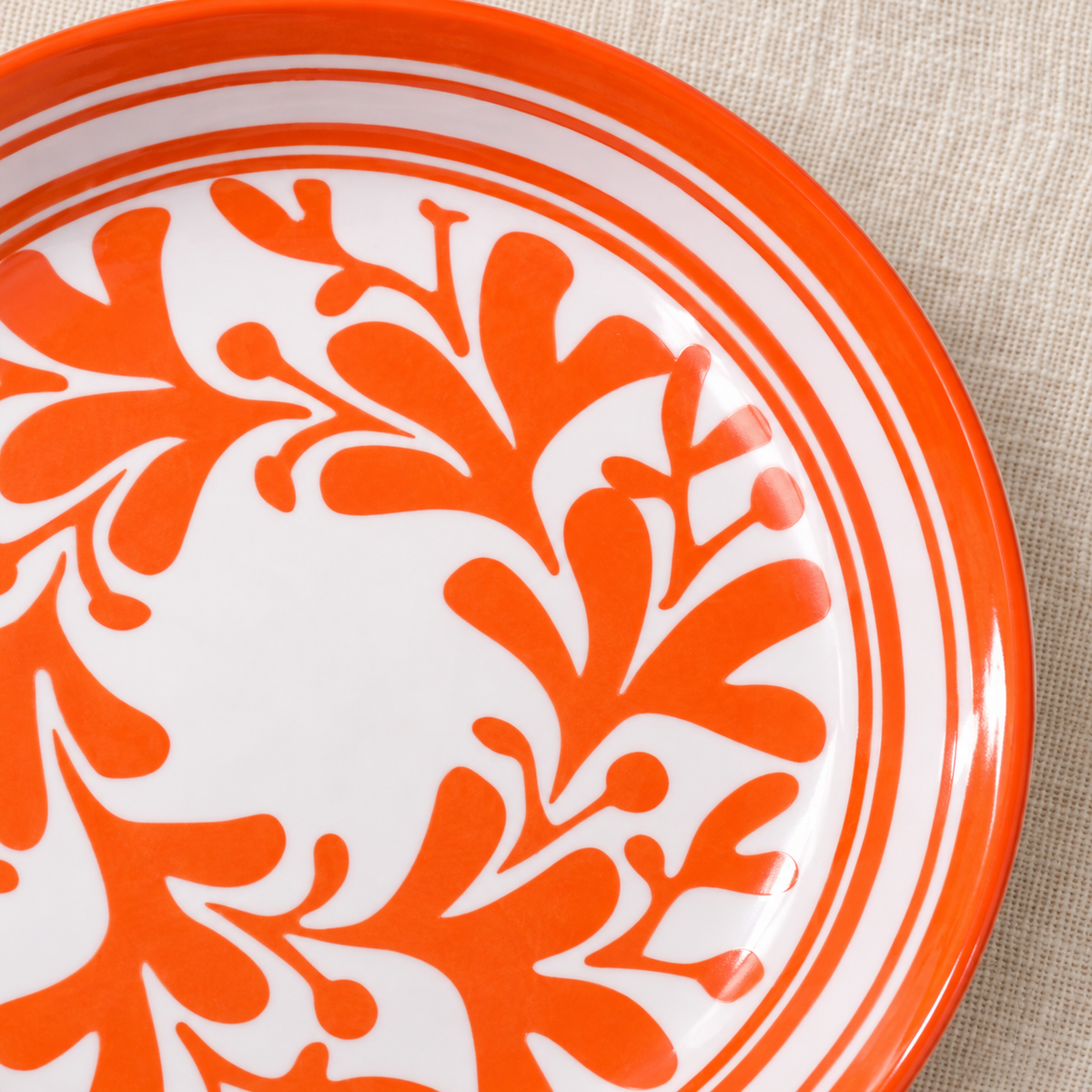 Close-up of the orange-patterned appetizer plate showing its motif and concentric rim structure. Food, linens and additional styling accessories are not included.