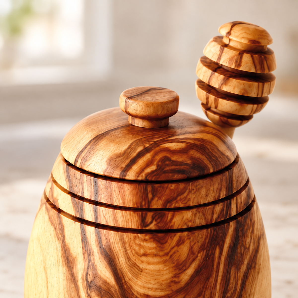 Cropped close-up of the olive wood honey pot's closed lid, knob and decorative shoulder grooves, with the matching dipper head behind.
