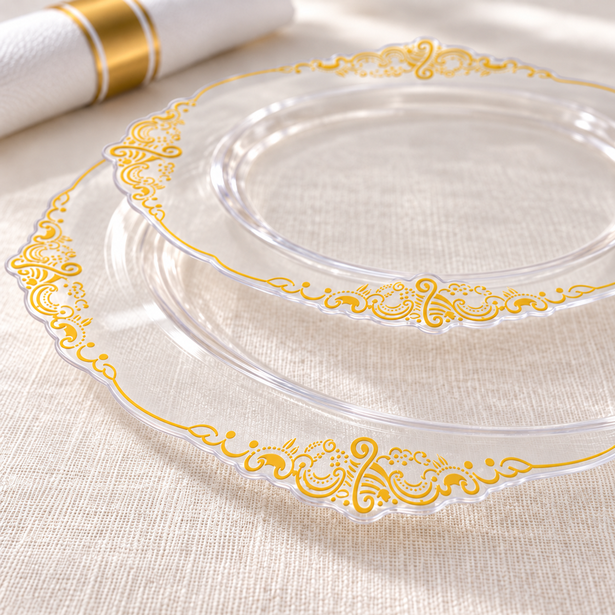 Close-up of clear plastic dinner and dessert plates showing the thin shaped edges and flat gold scroll print. Styling accessories are not included.