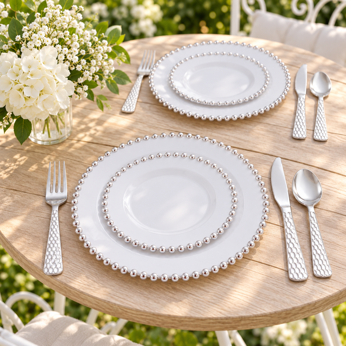 Silver pearl-edge plastic dinnerware and hammered-handle cutlery at an outdoor garden table. Flowers, furniture and decor are styling props, not included.