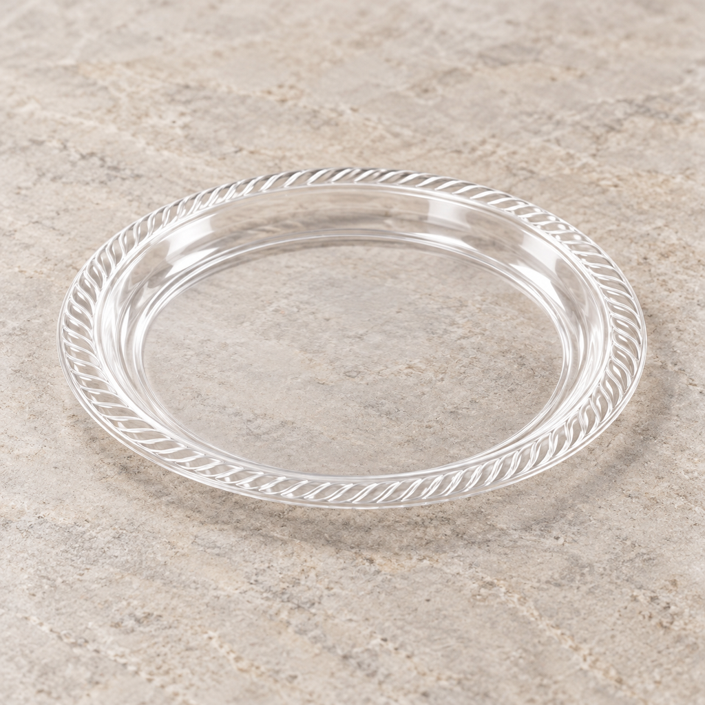 Clear round plastic plate with diagonal fluted rim. Empty angled view showing its shallow profile.