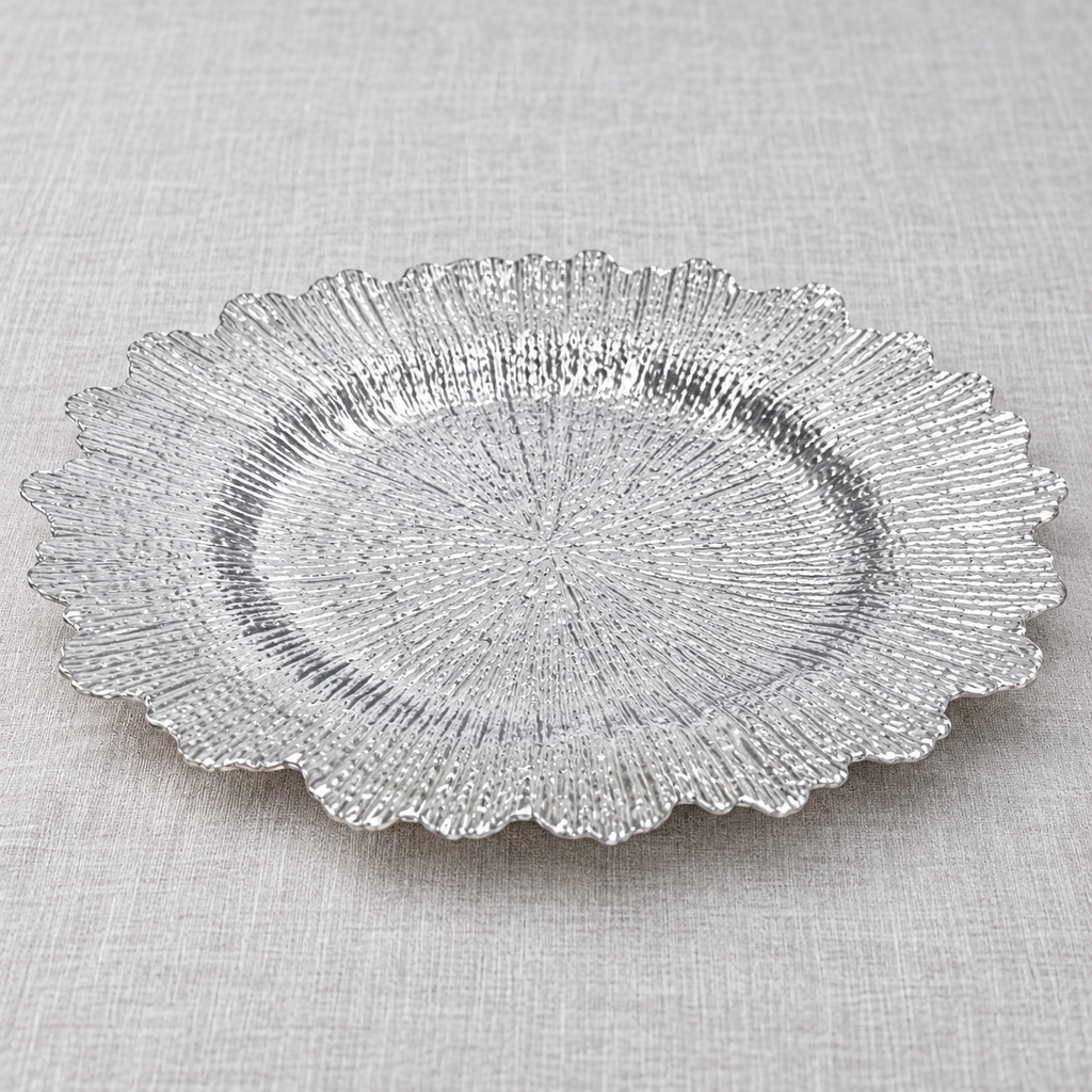 Silver ruffled charger with fine radial texture and an irregular scalloped perimeter. Empty low-angle view showing its shallow profile.