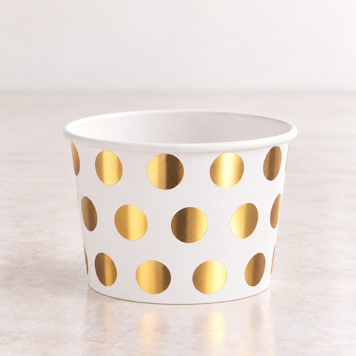 Close-up of a white paper dessert cup showing the large gold dot design, thin white rim and white interior.