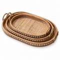 Three nesting rattan and wood serving trays with woven bases and loop handles on white