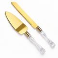 Gold-tone cake knife and server lying face up, with clear faceted plastic handles.