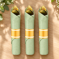 Representative gold-colored plastic cutlery rolls in sage green napkins with gold-and-white bands on a table