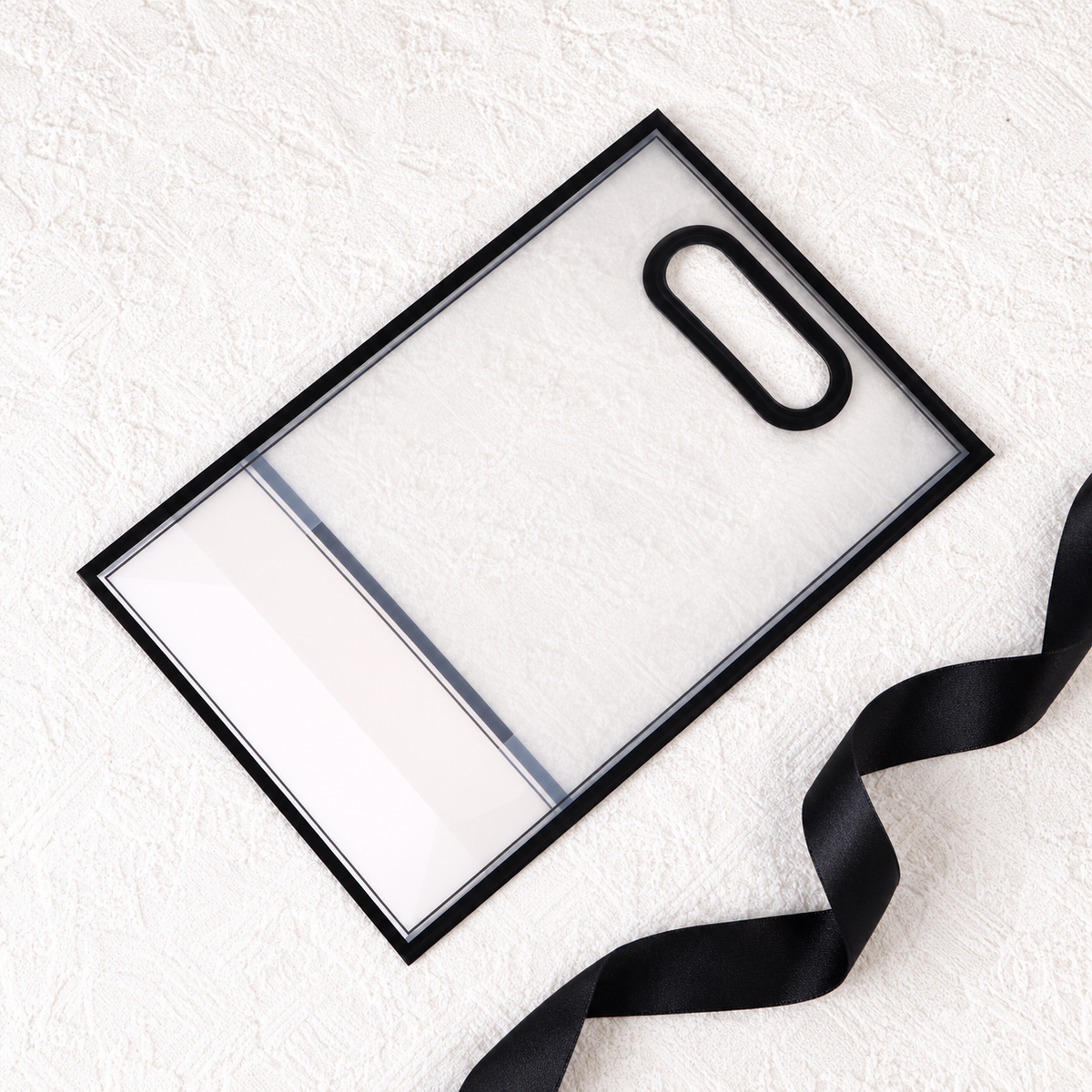 Flat clear black-edged gift bag with folded pale base and loose black ribbon