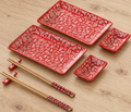 Red surname-pattern sushi set with two plates, two sauce dishes, two chopstick rests and two pairs of wooden chopsticks on an oak table