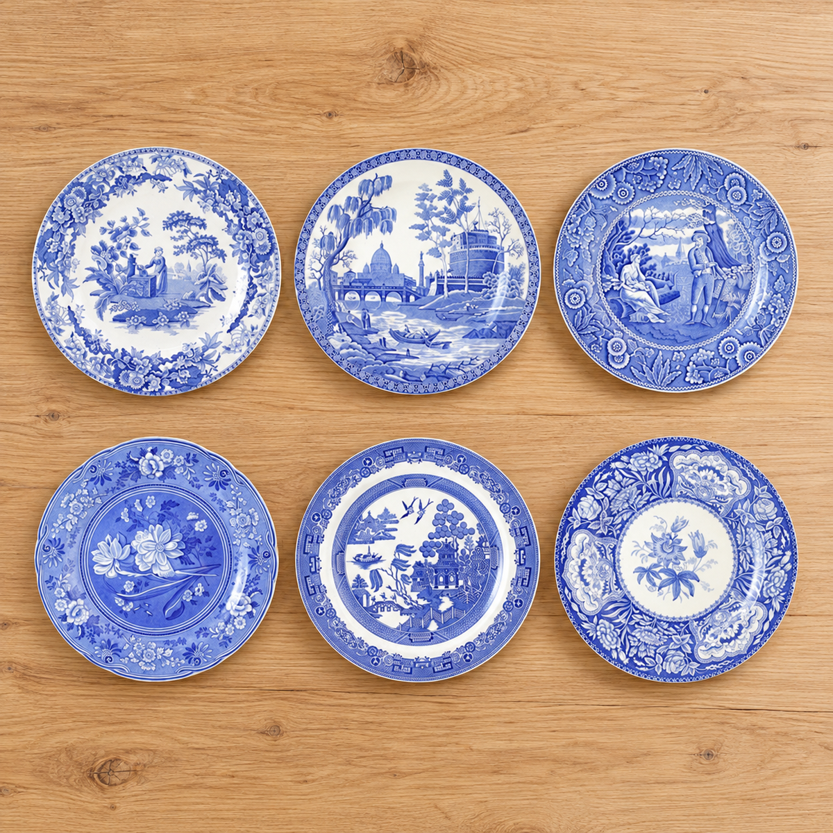 Six blue-and-white Spode Georgian dinner plates with distinct source designs displayed on an oak table